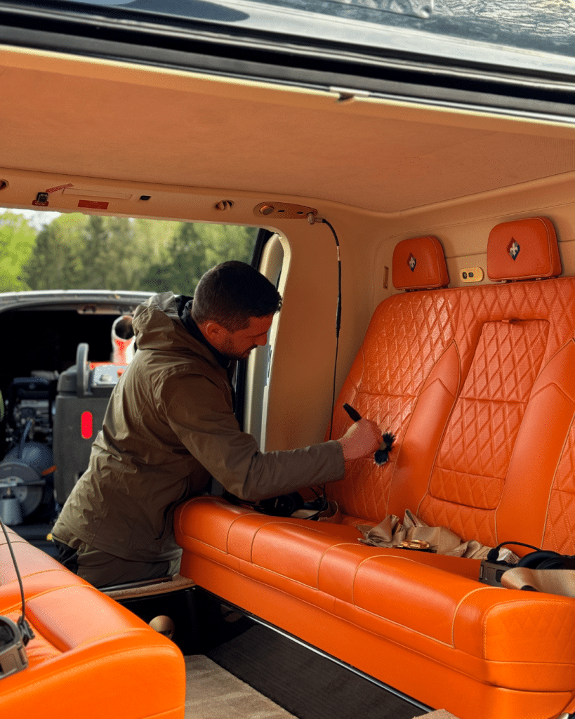 Professionelle Lederpflege im Fahrzeuginnenraum – Mitarbeiter reinigt orangefarbene Sitze.